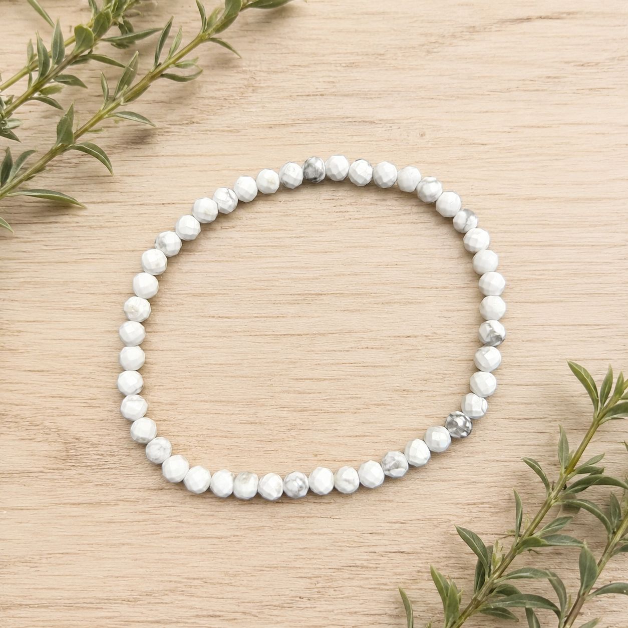 Faceted Howlite 4mm gemstone bracelet displayed on a light wooden table with greenery.