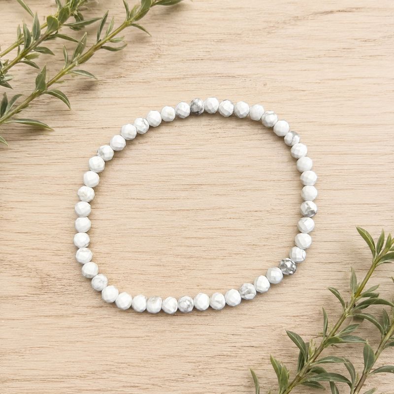 Faceted Howlite 4mm gemstone bracelet displayed on a light wooden table with greenery.
