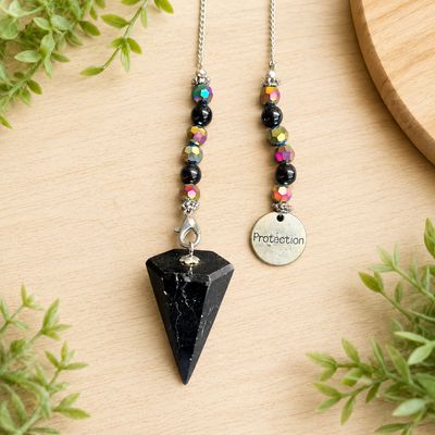 Close-up of a Black tourmaline protection pendulum with iridescent beads and silver charm on light wooden table