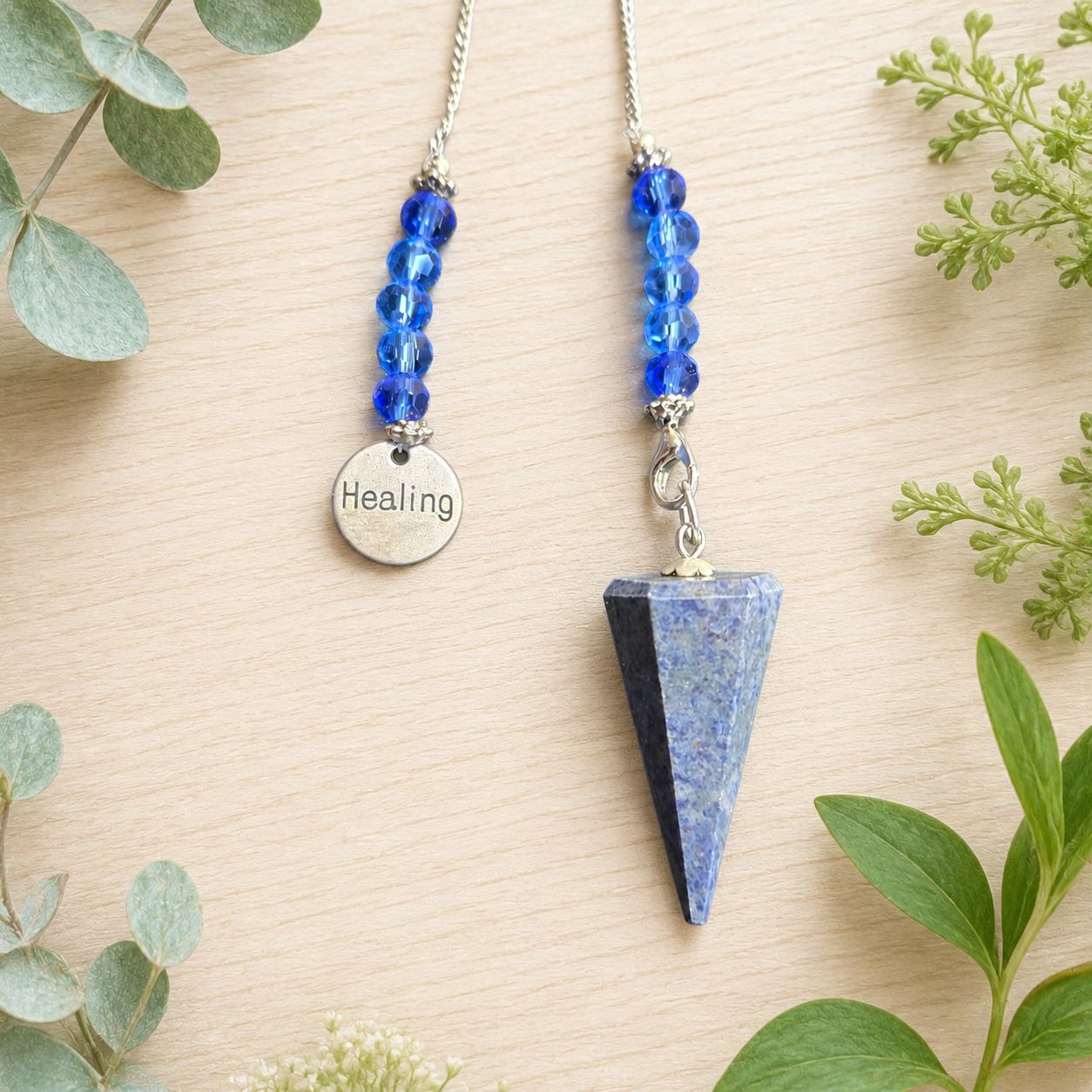 Close-up of a Dumortierite healing charm pendulum with blue beads and silver chain on light wooden table