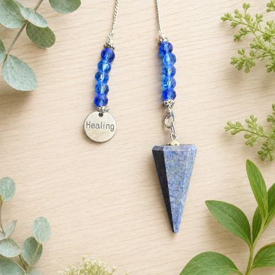 Close-up of a Dumortierite healing charm pendulum with blue beads and silver chain on light wooden table