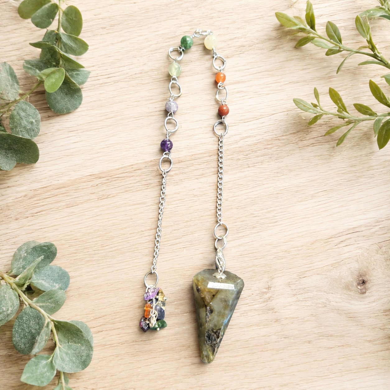 Labradorite chakra stones pendulum with colorful beads and silver chain on a light wooden table