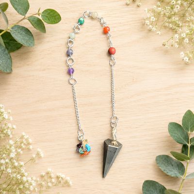 Pyrite chakra stones pendulum with colorful beads and silver chain on a light wooden table