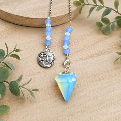 A close-up of an opalite celestial pendulum with blue beads and silver sun and moon charm on light wooden table