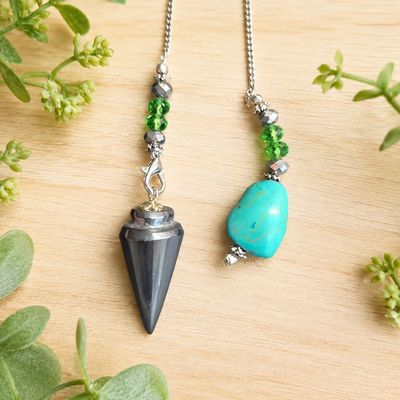 Close-up of a hematite pendulum with turquoise nugget, green beads, and silver chain on a light wooden table