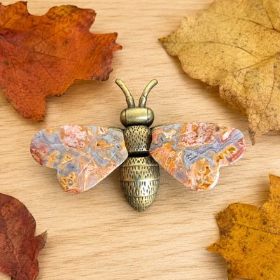 Crazy Lace Agate metal bee with gemstone wings displayed on a light wooden table with fall leaves.