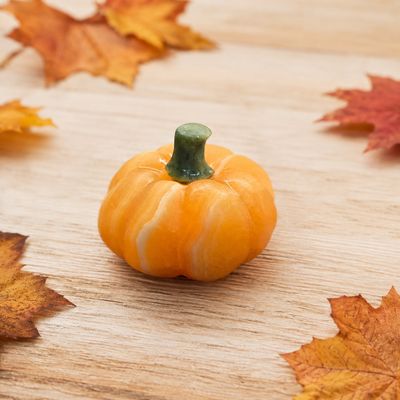 Orange Calcite pumpkin carving on a light wooden table with autumn leaves