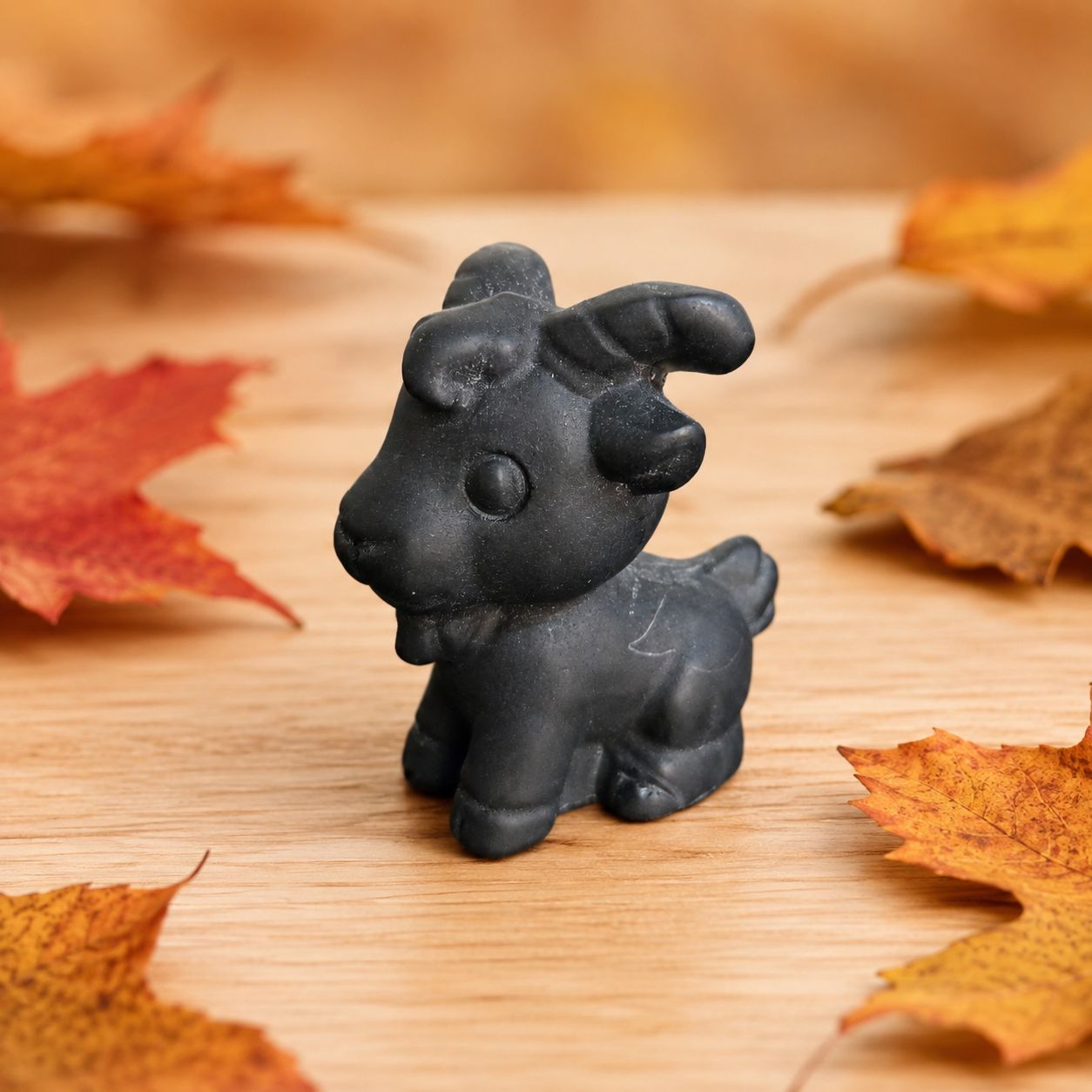 Black Obsidian goat carving displayed on a light wooden table with autumn leaves