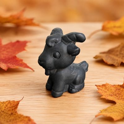 Black Obsidian goat carving displayed on a light wooden table with autumn leaves