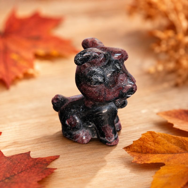 Garnet goat carving displayed on a light wooden table with autumn leaves