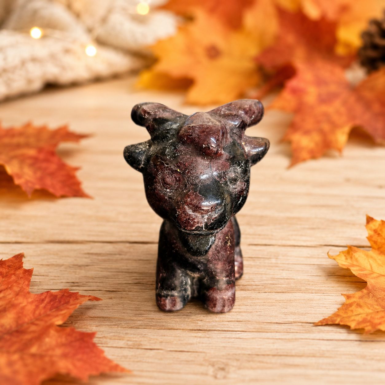 Front profile of a garnet goat carving displayed on a light wooden table with autumn leaves