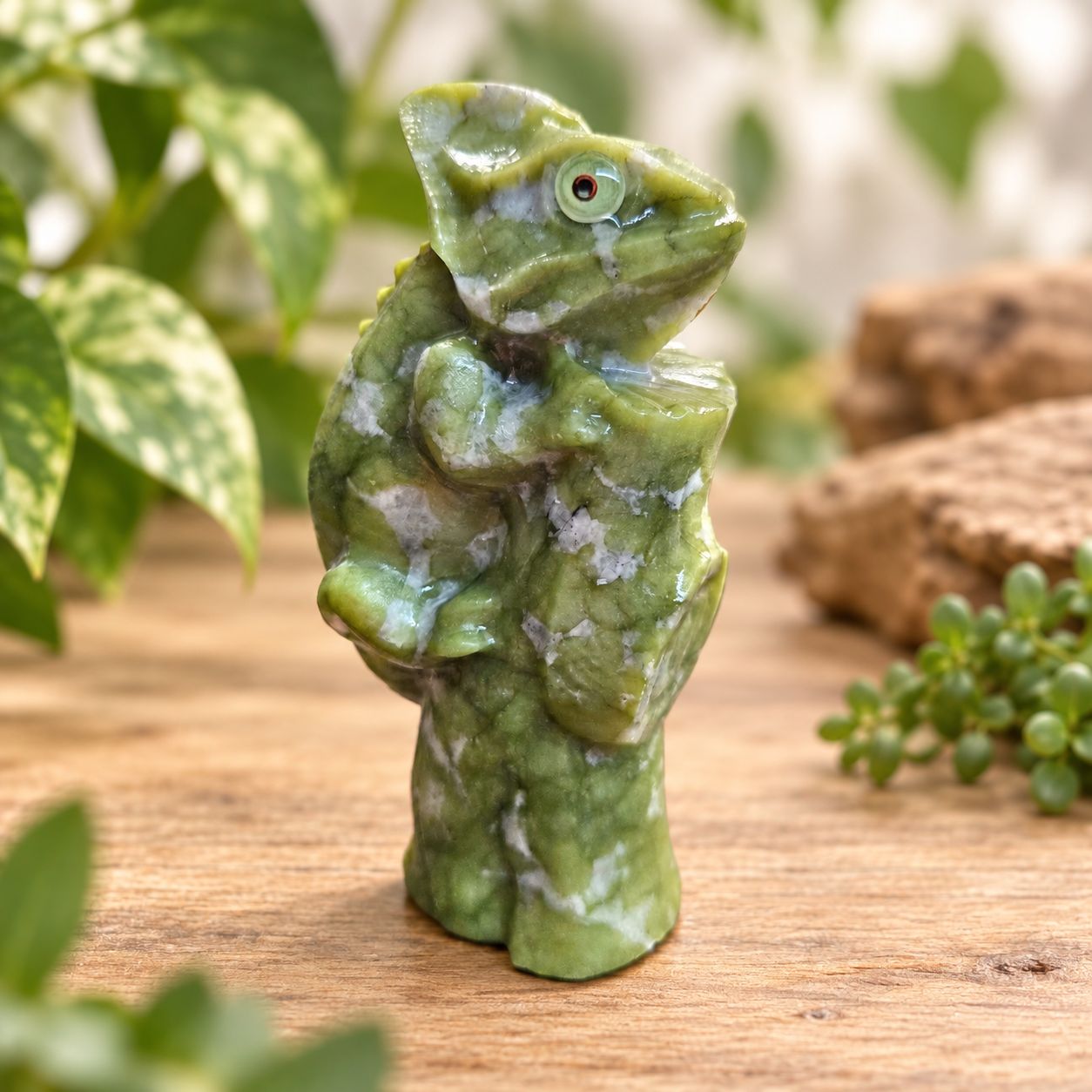 Serpentine chameleon carving displayed on a light wooden table with greenery.