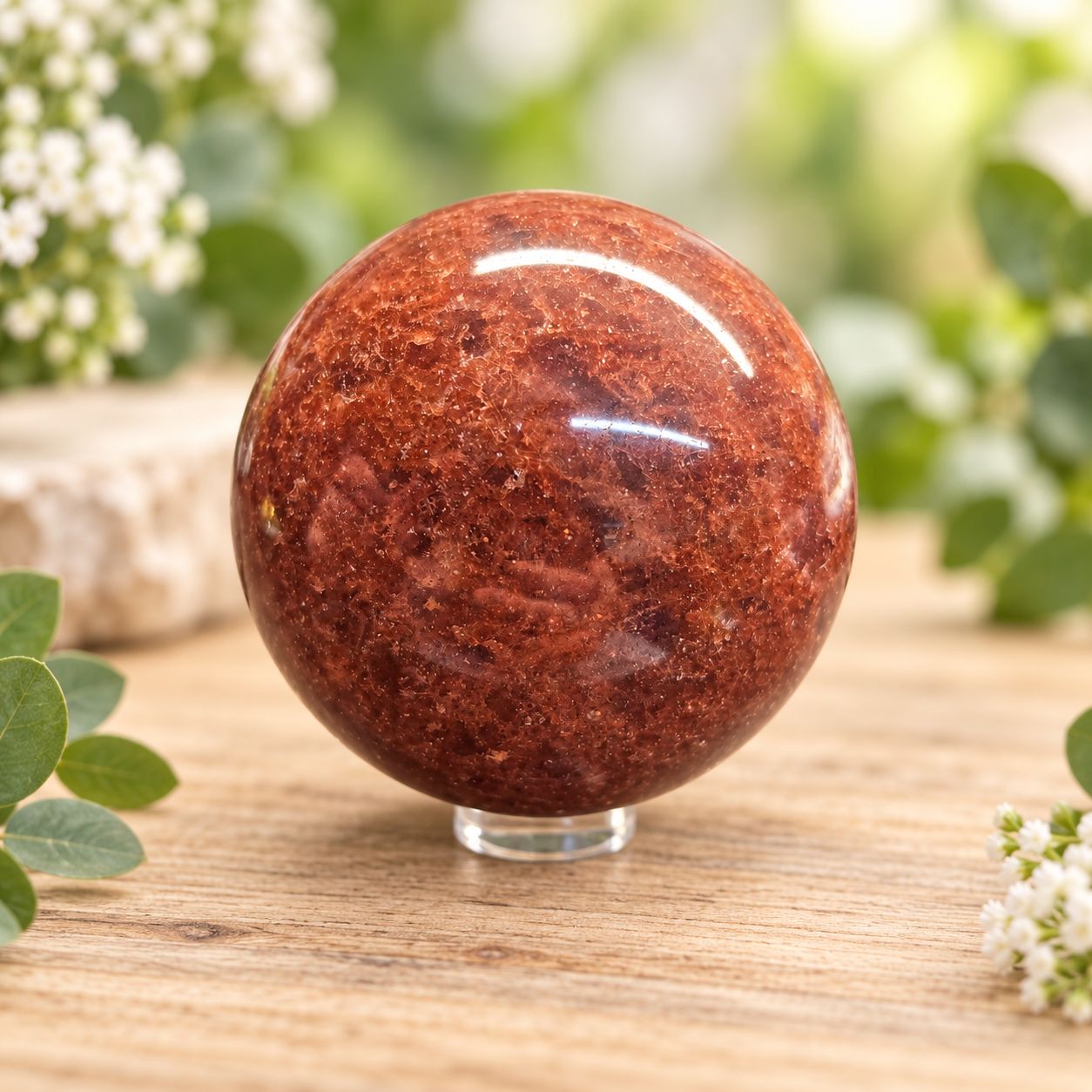 Medium Strawberry Quartz sphere with rich reddish-pink tones on a light wooden table with greenery.
