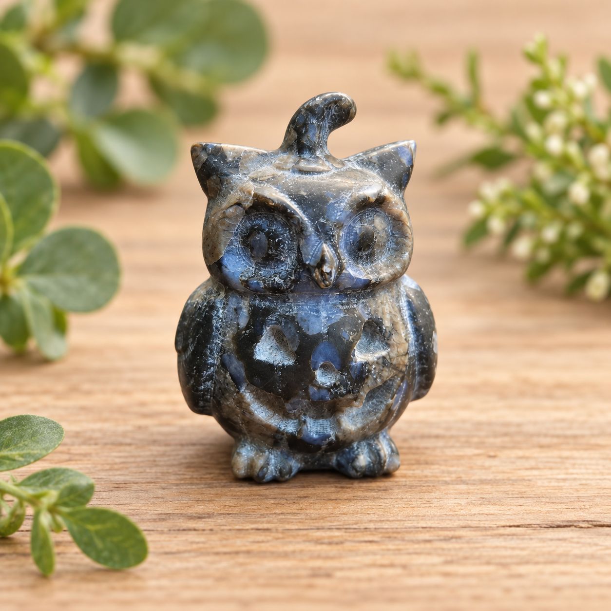 Front view of Blue Que Sera pumpkin owl carving on a light wooden table with greenery