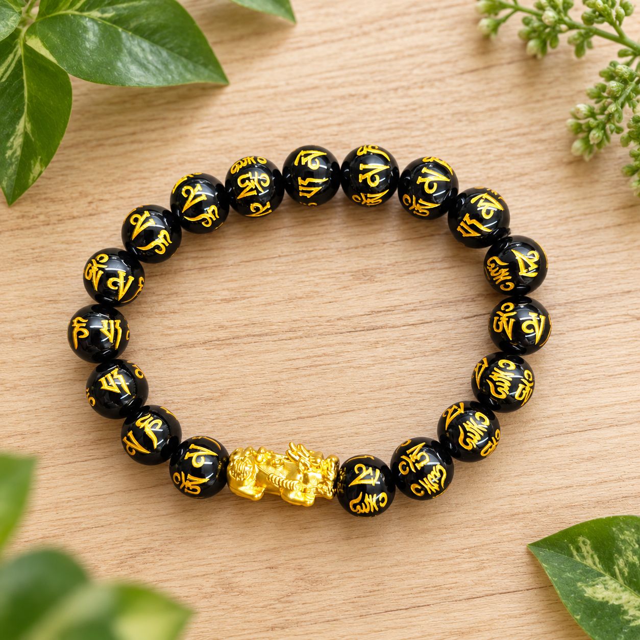Golden Pixiu 10mm onyx bracelet with gold markings on a light wooden table with greenery