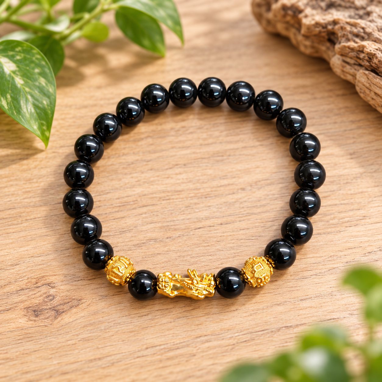 Golden Pixiu 8mm obsidian bracelet displayed on a light wooden table with greenery