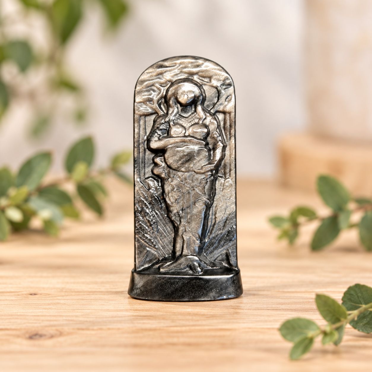 Silver Sheen Obsidian Gaia carving displayed on a light wooden table with greenery