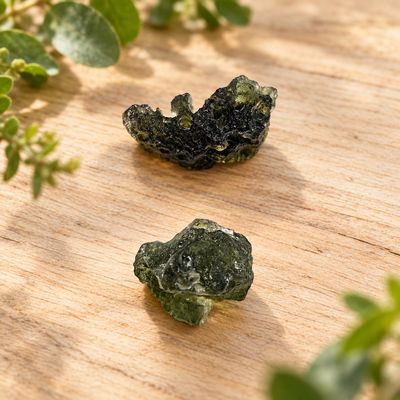 Natural Moldavite specimens on a light wooden table with greenery.