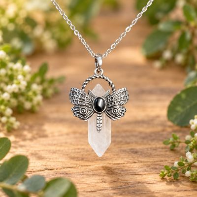 Quartz dragonfly point necklace with silver-tone pendant and stainless steel chain on light wood with greenery.