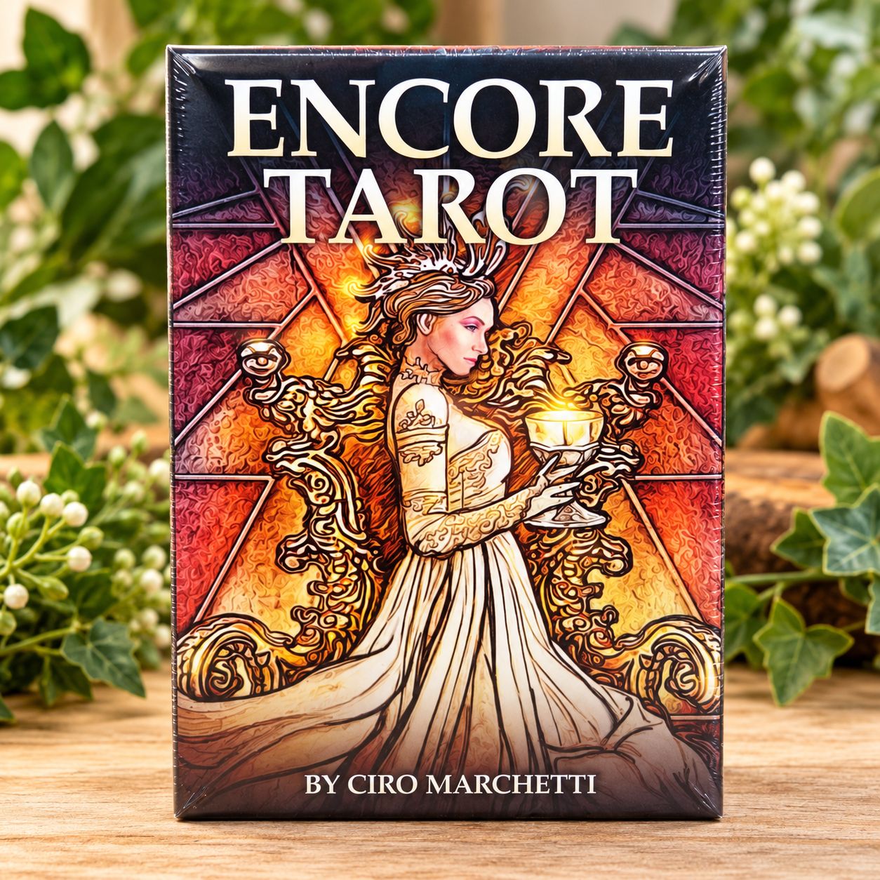 Encore Tarot deck by Ciro Marchetti displayed upright on a light wooden table with soft greenery in the background.
