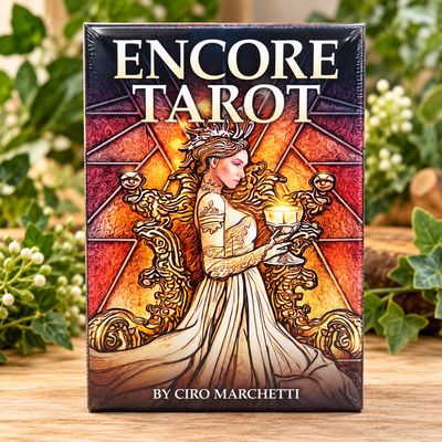 Encore Tarot deck by Ciro Marchetti displayed upright on a light wooden table with soft greenery in the background.