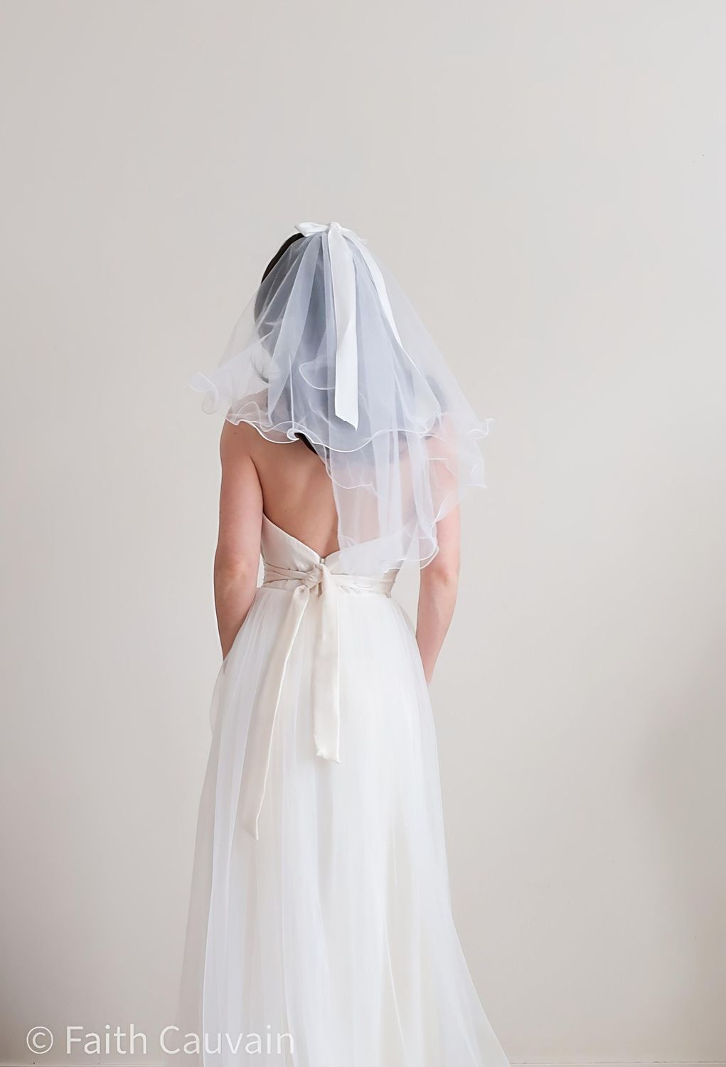 Voile de mariée court en tulle fin, orné d’un élégant nœud à l’arrière, porté avec une robe de mariée moderne.
