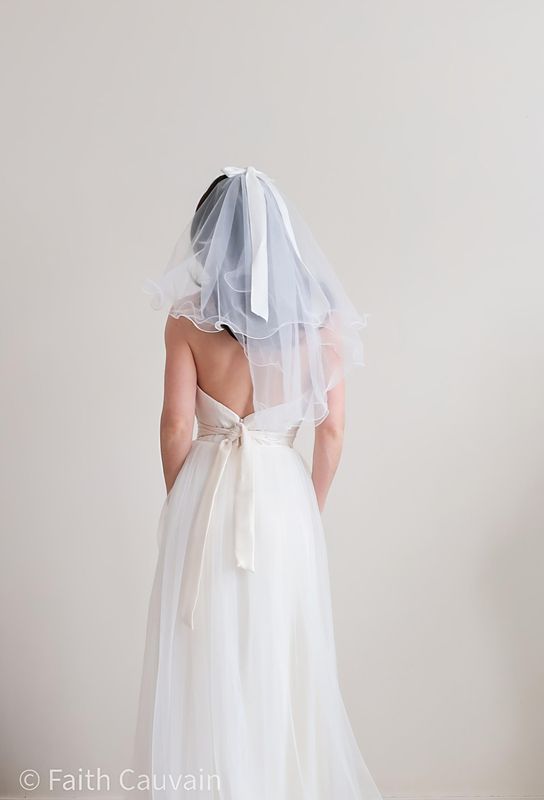 Voile de mariée court en tulle fin, orné d’un élégant nœud à l’arrière, porté avec une robe de mariée moderne.
