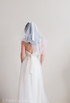Voile de mariée court en tulle fin, orné d’un élégant nœud à l’arrière, porté avec une robe de mariée moderne.
