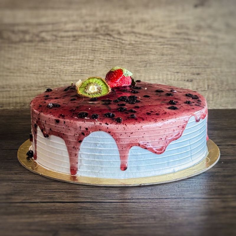 a round ice cream cake with blueberry sauce on top, decorated with a kiwi and strawberry
