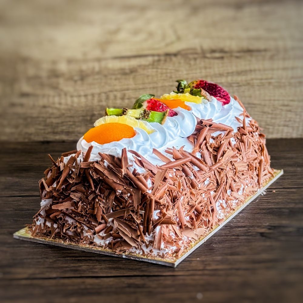 an ice cream cake in log shape, covered with chocolate flakes and fresh fruits on top.