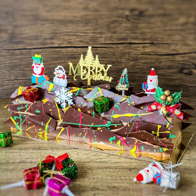 a Christmas Log Cake - Dubai filling and chocolate ganaches decorations, topping with various xmas figure decorations