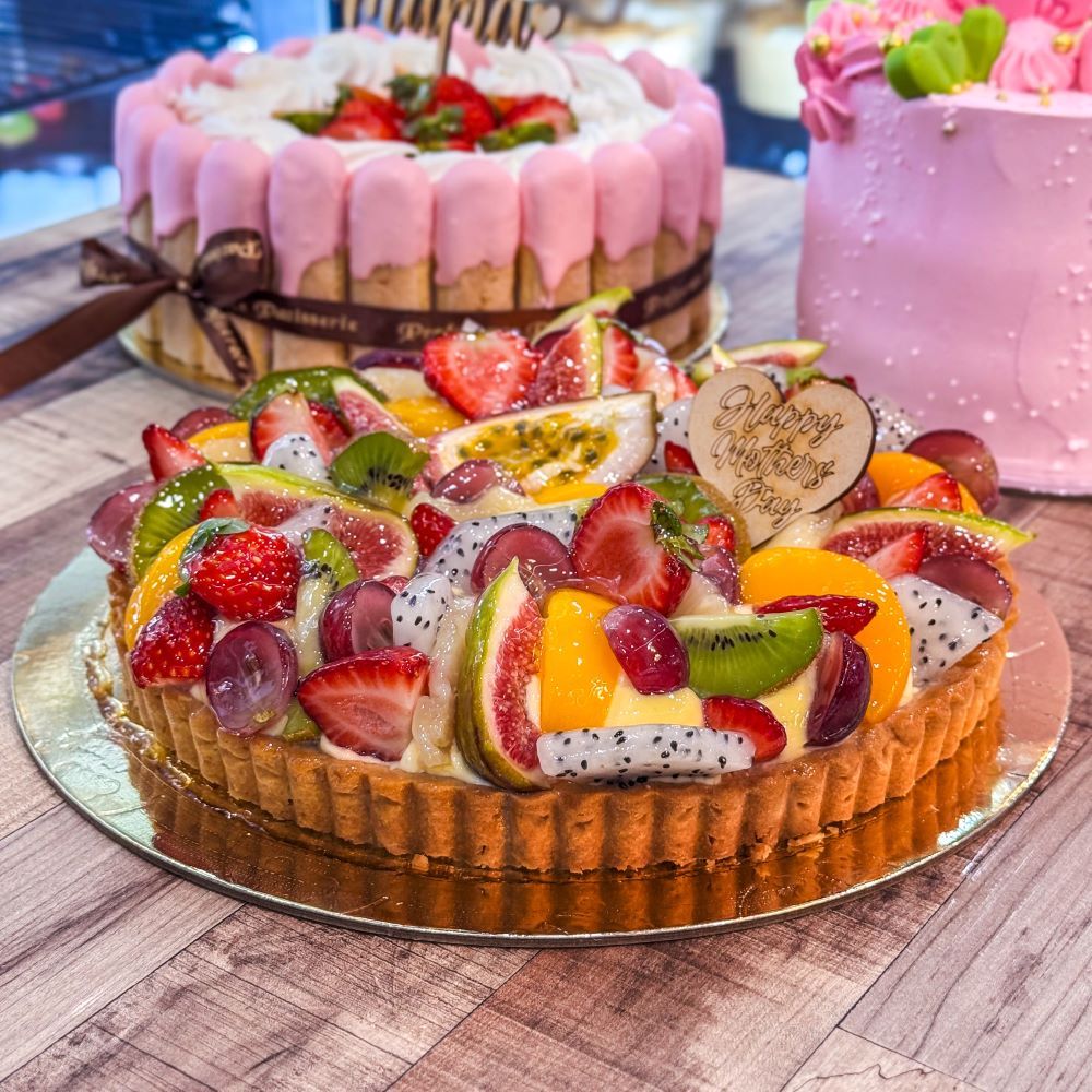 a Mother's Day Cake - Exotic Tart, made from a vibrant mix of strawberries, passionfruit, fig, pineapple, peach, kiwi, grapes, and dragonfruit on a bed of creamy custard in a crisp tart shell. Fresh, colourful, and full of flavour.