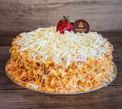 a white forest cake with almond around and topped with white chocolate finishes