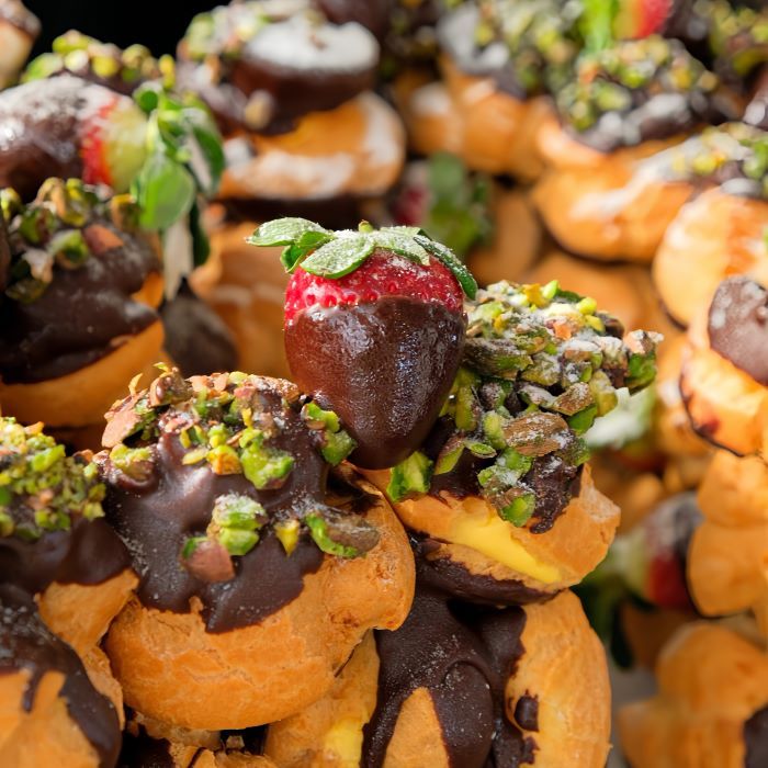 profiterole single letter cake with pistachio and strawberries on top