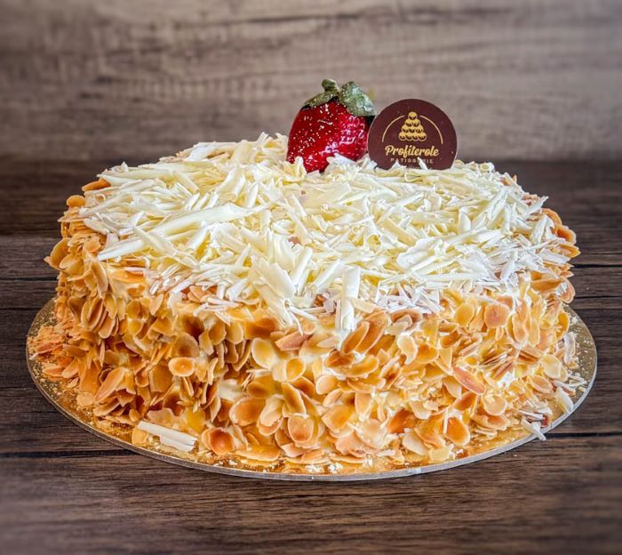a white forest cake with almond around and topped with white chocolate finishes
