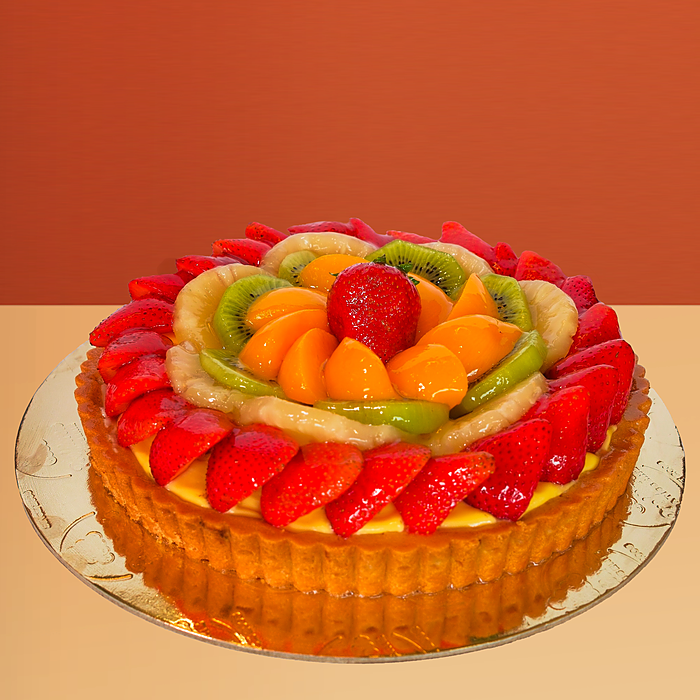 Round fresh fruit cake with glazed strawberries kiwi mango and banana slices arranged on a golden pastry base by Profiterole 