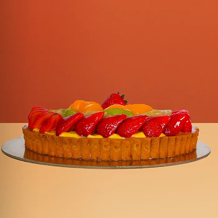 Round fresh fruit cake with glazed strawberries kiwi mango and banana slices arranged on a golden pastry base by Profiterole 