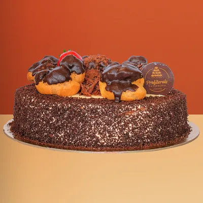 Chocolate profiterole cake covered in chocolate sprinkles with chocolate-dipped profiteroles and a fresh strawberry on top 