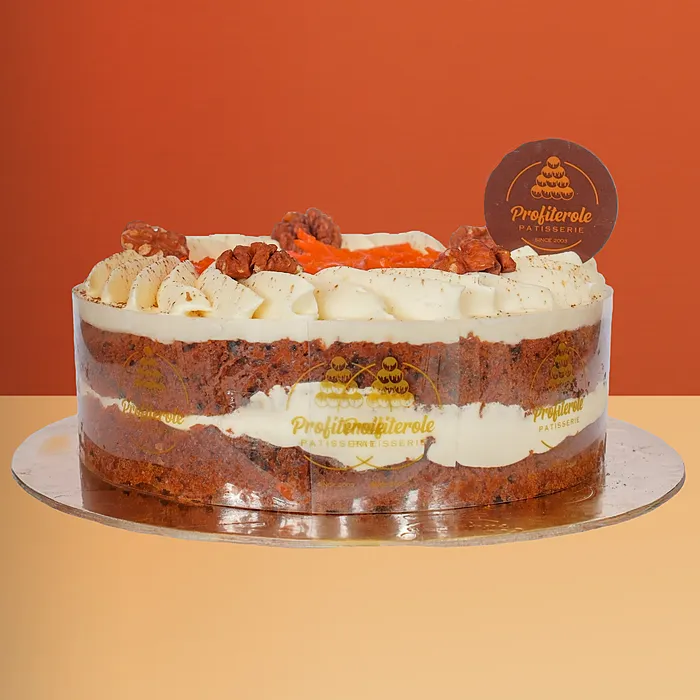 Carrot cake with semi-naked cream frosting showing sponge layers topped with shredded carrot walnuts and cream by Profiterole