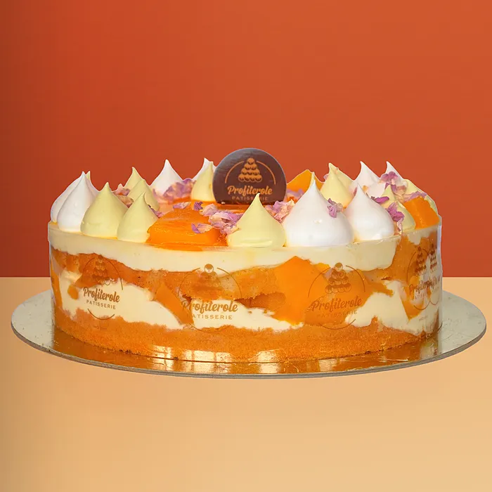 Mango Cake Fresh mango cake with mango cream layers visible through the sides topped with cream dollops and flower petals by Profiterole