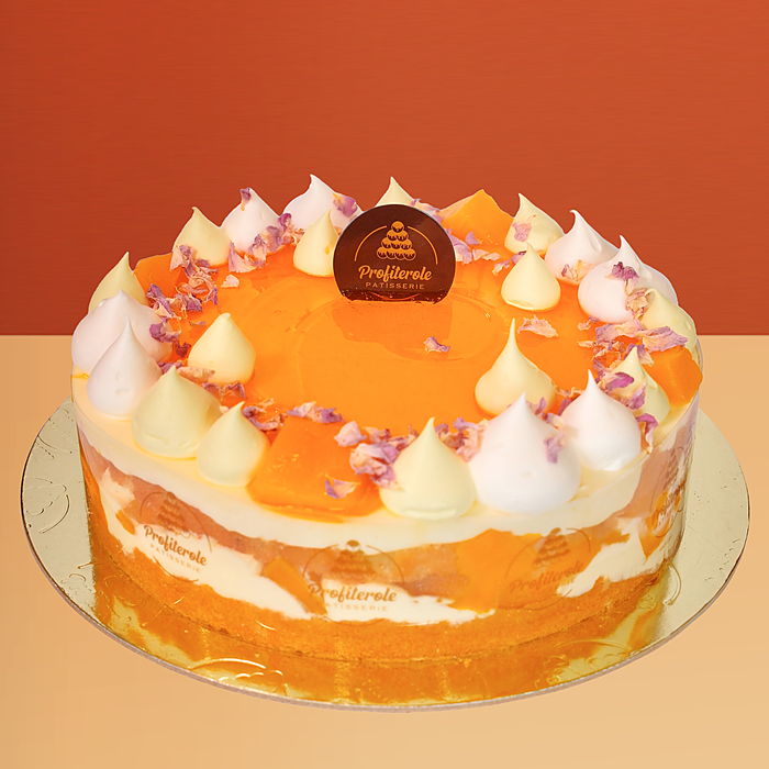 Fresh mango cake with mango cream layers visible through the sides topped with cream dollops and flower petals by Profiterole