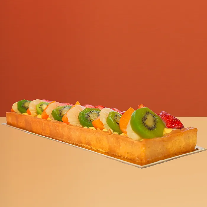 Log-shaped fresh fruit cake w/ rows of kiwi strawberry & mango on a golden pastry base by Profiterole Patisserie