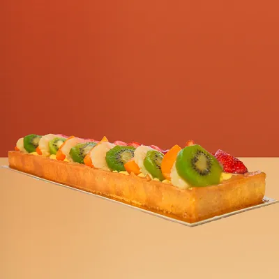 Log-shaped fresh fruit cake w/ rows of kiwi strawberry & mango on a golden pastry base by Profiterole Patisserie