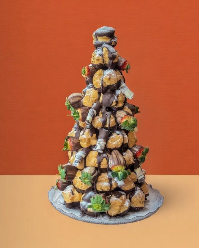 Profiterole Tower Croquembouche profiterole tower with dark chocolate, strawberries, and white chocolate curls on and orange and beige backgrou