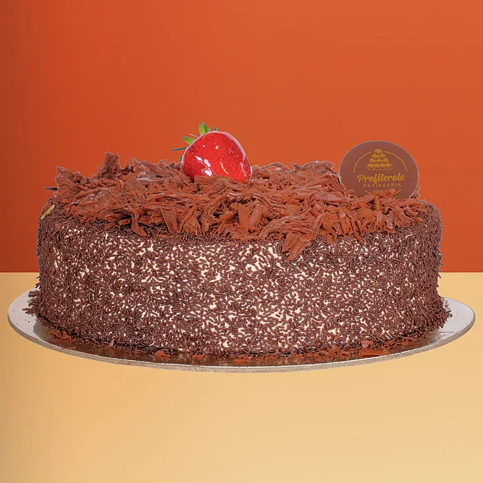 Black forest cake covered in chocolate shavings and flakes with a fresh strawberry on top by Profiterole Patisserie