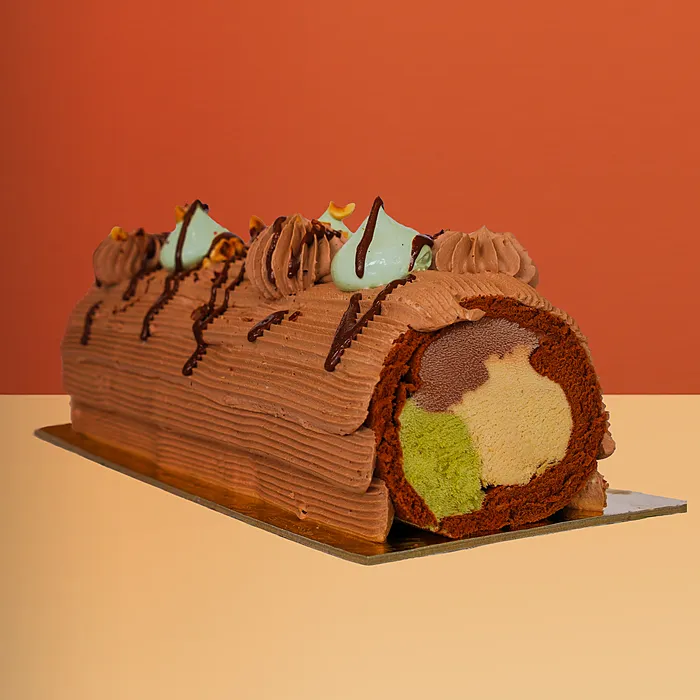 Chocolate Swiss roll ice cream cake with chocolate ganache piping showing hazelnut pistachio and chocolate gelato inside