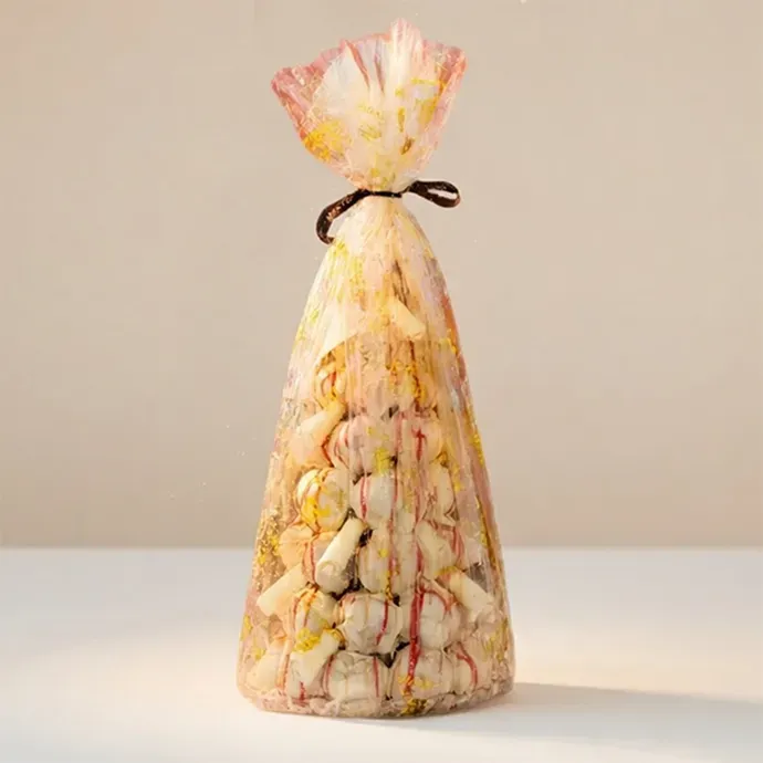 white profiterole tower wrapped in a think film the vanilla filled and white chocolate dipped profiteroles are visible