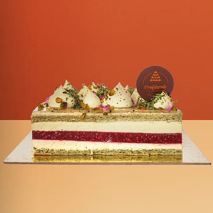 Pistachio raspberry bliss cake with pistachio cream, raspberry layers, cream dollops & crushed pistachios by Profiterole