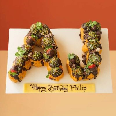 Profiterole letter cake shaped as AJ with chocolate, pistachios, and strawberries