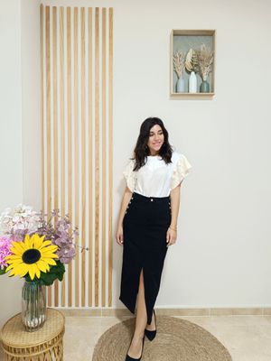 Falda con silueta tubo, en color nagro y tejido denim, adornada con botones dorados en el filo de los bolsillos delanteros y con abertura central por delante